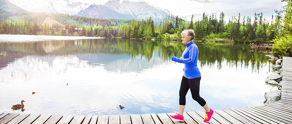 A senior adult exercising outside by a lake and mountains